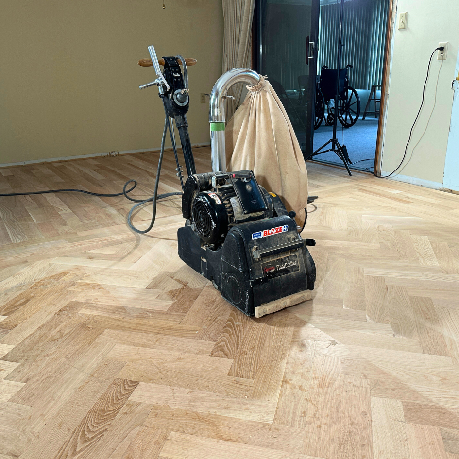 A belt sander with a canvas dust collection bag attached sitting on new installation of herringbone white oak in St. Joseph Michigan. 