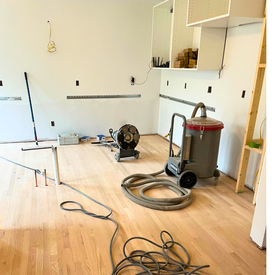 A hardwood refinishing dust containment vacuum sitting on a newly installed red oak floor with a buffer next to it.