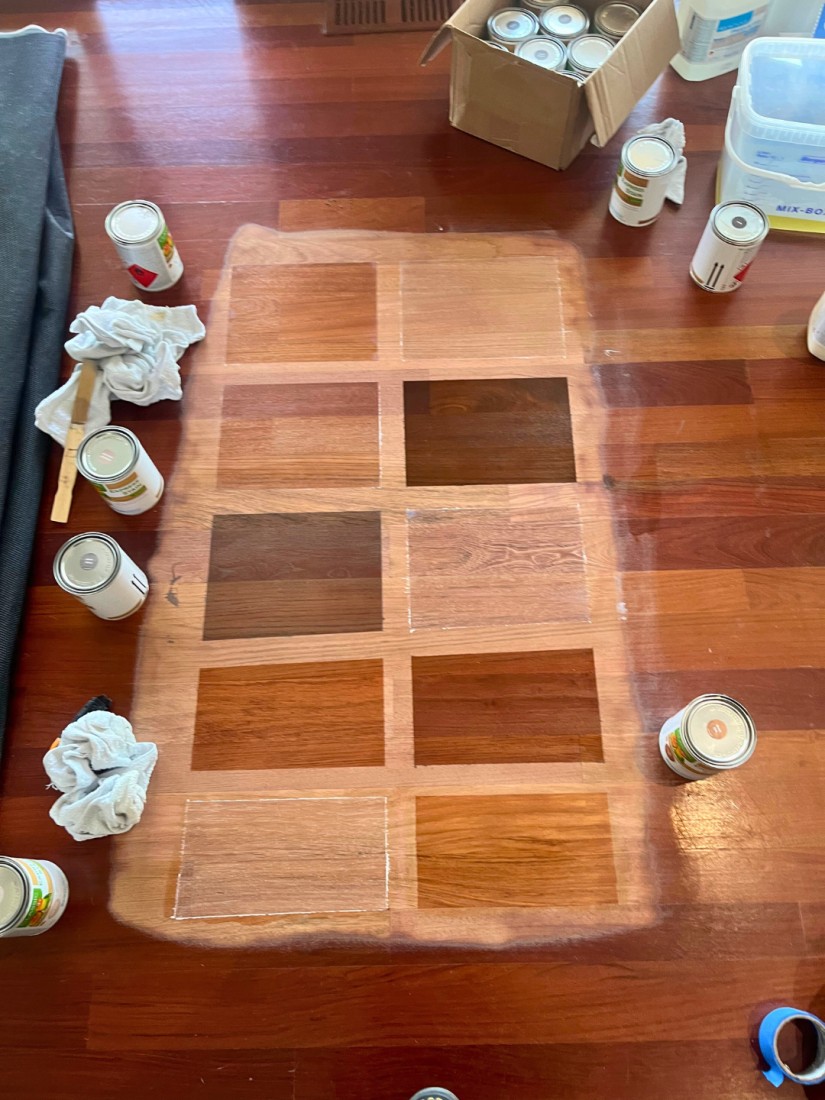 A Brazilian Cherry wood floor with multiple, brown, white and dark stain samples on it. 